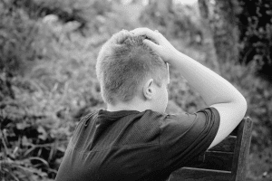 Jovem de costas com a mão na cabeça, simbolizando angústia ou a ausência paterna.