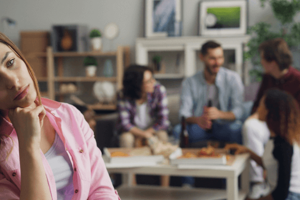 Mulher adulta pensativa e desconectada em um ambiente social, representando conflitos emocionais ligados ao cérebro adolescente e à formação da identidade adulta.