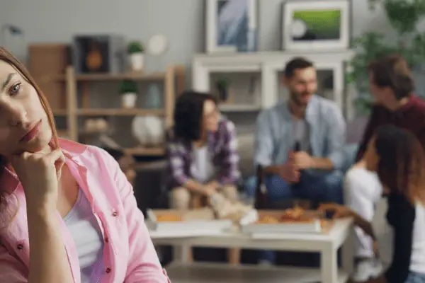 Mulher adulta pensativa e desconectada em um ambiente social, representando conflitos emocionais ligados ao cérebro adolescente e à formação da identidade adulta.